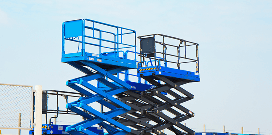Two blue scissor lifts outside of a facility