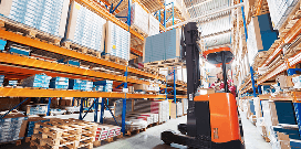 Orange forklift placing a package on a high shelf in a warehouse facility