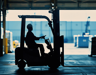 A worker drives a forklift in front of a bay door in a warehouse