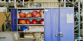 Storage cabinet in a warehouse containing safety helmets, paperwork, and protective gear.