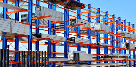 A large blue and orange cantilever rack holding industrial stock supplies outside