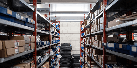 Rows of red shelves holding various automotive parts and packages with a stack of tires in the background