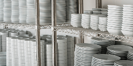 Two wire shelving units holding stacks of white plates and bowls