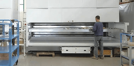 A worker uses a large vertical lift system in a warehouse with shelving racks in the foreground