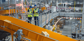 Two warehouse supervisors reviewing operations on an elevated platform above a conveyor system in a distribution center.