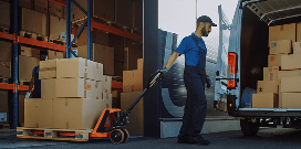 Warehouse worker using a pallet jack to move boxes from storage racks to a delivery van.